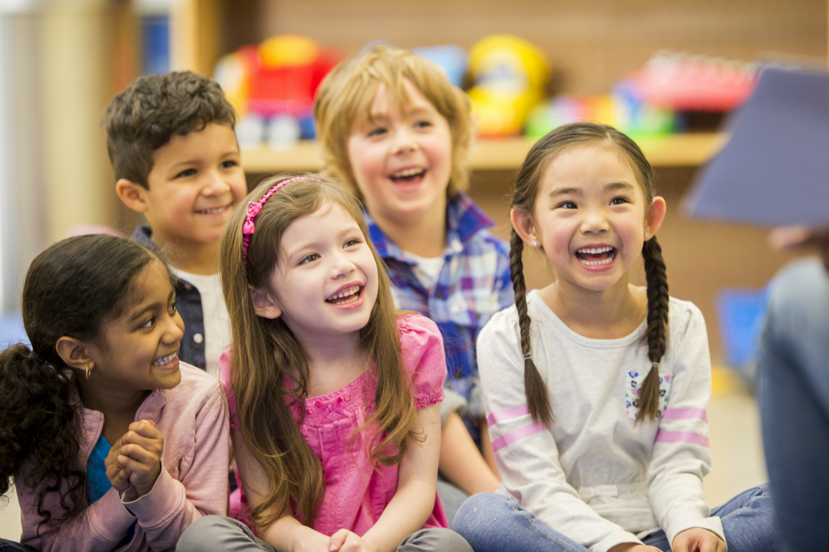A group of diverse young children laugh and enjoy stories